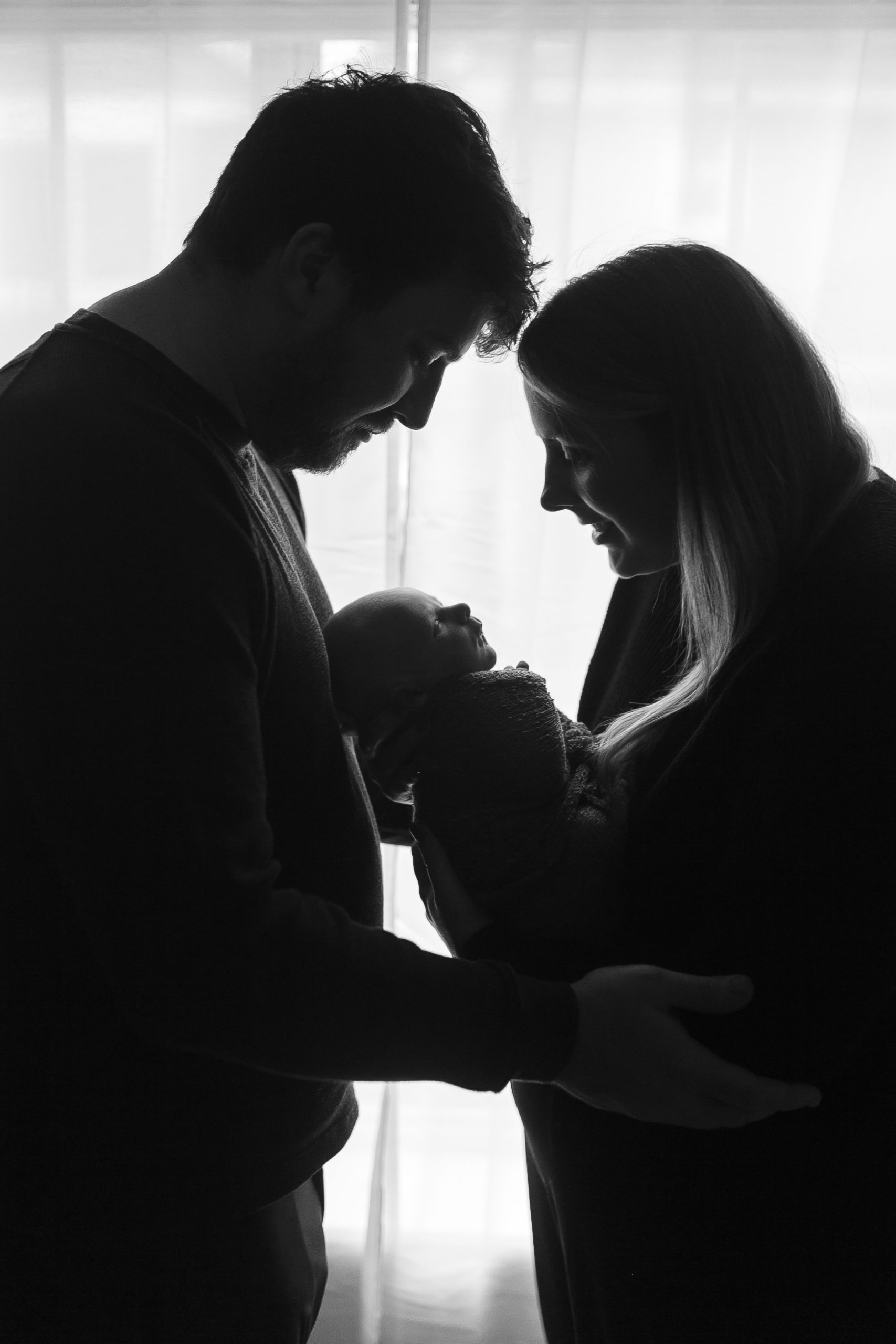In-home Lifestyle newborn session A silhouette of a couple holds their newborn baby during their in-home lifestyle newborn session.